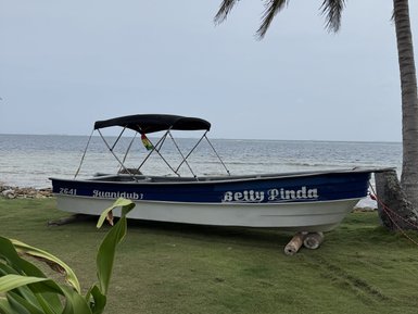 Ein Motorboot mit dem Namen 'Betty Linda' steht an einem Strand, umgeben von sanften Wellen und grünen Pflanzen.