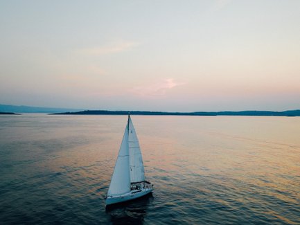 Ein Segelboot gleitet sanft über das ruhige Wasser, während der Himmel in sanften Pastellfarben leuchtet.