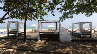 Ein entspannender Strandbereich mit eleganten Liegen und Sonnenschirmen, umgeben von sanften Wellen und strahlendem Himmel.