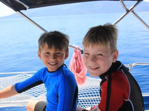 Zwei fröhliche Jungen in Neoprenanzügen sitzen auf einem Boot und genießen die Sonne und das Wasser um sie herum.