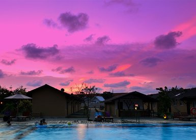 Ein Pool mit glitzerndem Wasser spiegelt den atemberaubenden pinken Sonnenuntergang über einem Resort wider.