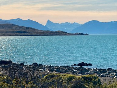 Der glitzernde Lago Argentino spiegelt die majestätischen Berge im Hintergrund wider, während sanfte Wellen das Ufer umspielen.