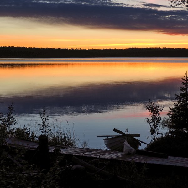 Ein ruhiger Abend am See, wo sanfte Wellen das orangefarbene Licht des Sonnenuntergangs reflektieren.