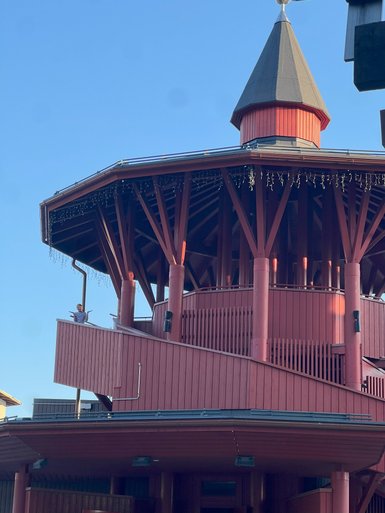 Ein rotes, mehrstöckiges Gebäude mit einem spitzen Dach, das von einem klaren blauen Himmel umgeben ist.