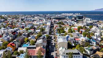 Ein Blick auf Reykjavik zeigt bunte Häuser und eine belebte Straße, die zum Hafen führt, unter strahlend blauem Himmel.