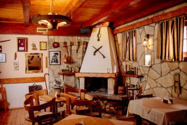 Ein rustikales Restaurant mit Holzmöbeln, einem offenen Kamin und dekorativen Werkzeugen an den Wänden.