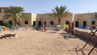 Ein sonniger Innenhof mit Palmen, Spielgeräten und farbenfrohen Gebäuden, die eine entspannte Atmosphäre schaffen.