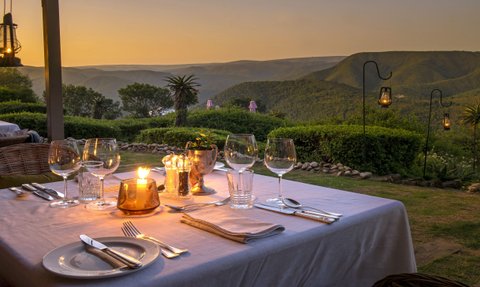Ein romantisch gedeckter Tisch im Freien, beleuchtet von Kerzen, mit Blick auf die Berge bei Sonnenuntergang.