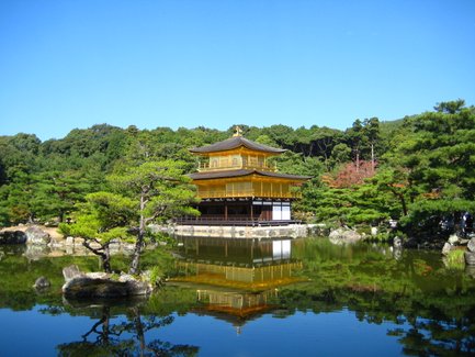 Der Goldene Pavillon in Kyoto spiegelt sich majestätisch im ruhigen Wasser eines Teiches, umgeben von üppigem Grün.