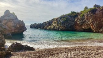 Eine ruhige Bucht mit klarem, türkisfarbenem Wasser, umgeben von steilen Felsen und sanften Wellen am Strand.