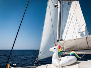 Ein auf einem Segelboot schwimmendes, aufblasbares Einhorn vor einem klaren blauen Himmel und dem weiten Meer.