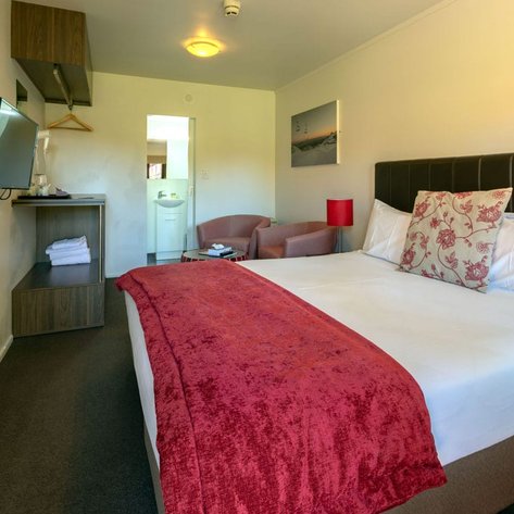 Ein gemütliches Hotelzimmer mit einem großen Bett, einem roten Überwurf und einem Fernseher an der Wand.