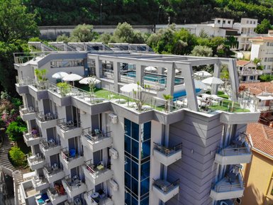Das moderne Hotel in Budva hat eine Dachterrasse mit Pool und Sonnenschirmen, umgeben von üppigem Grün und bunten Blumen.