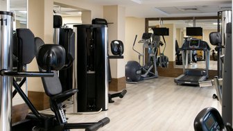 Ein modernes Fitnessstudio mit verschiedenen Trainingsgeräten, darunter Laufband und Kraftmaschinen, in einem hellen Raum.