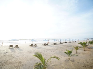 Ein ruhiger Strand mit Liegen und Sonnenschirmen, während Menschen am Wasser spazieren und die Wellen genießen.
