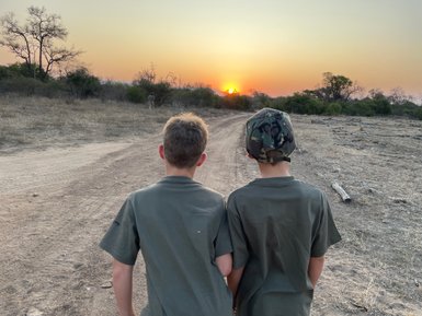 Zwei Kinder blicken auf einen farbenfrohen Sonnenuntergang in Makutsi – Südafrika Reise mit Kindern