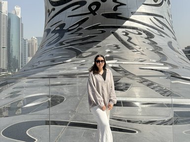 Eine Frau steht auf einer modernen Plattform mit reflektierender Oberfläche, umgeben von futuristischer Architektur und Wolkenkratzern.