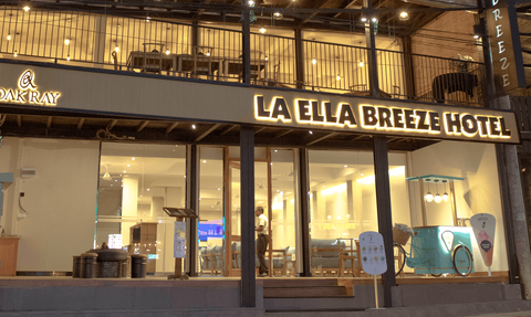 Die Fassade des La Ella Breeze Hotels zeigt eine einladende Atmosphäre mit warmem Licht und modernen Möbeln im Innenbereich.