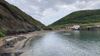 Eine ruhige Küstenlandschaft mit sanften Hügeln, einem Sandstrand und Menschen, die sich am Wasser entspannen.
