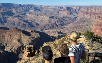 Drei Kinder stehen am Rand des Grand Canyon und bewundern die beeindruckende Aussicht auf die tiefen Schluchten und Felsen.