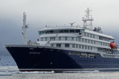 Das Schiff 'Hondius' liegt majestätisch im Wasser, umgeben von Eis und einer dramatischen, bewölkten Landschaft.