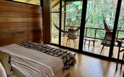 Ein gemütliches Schlafzimmer mit einem großen Bett und einem Blick auf eine grüne, tropische Terrasse mit Hängestühlen.