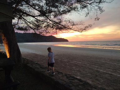 Kind genießt den Sonnenuntergang am Strand des Nexus Resorts – Malaysia & Borneo Reise mit Kindern