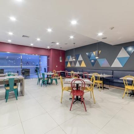 Ein modernes Restaurant mit bunten Stühlen und geometrischen Wanddekorationen, das eine einladende Atmosphäre schafft.