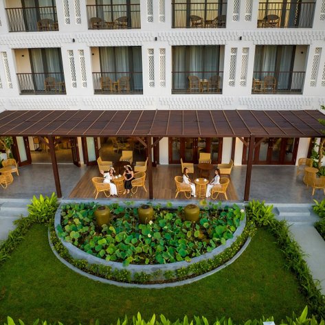 Eine Gruppe von Frauen sitzt entspannt unter einem Holzüberstand und genießt Getränke in einem eleganten Gartenbereich.