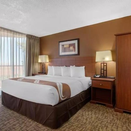 Ein gemütliches Hotelzimmer mit einem großen Bett, warmen Farben und viel natürlichem Licht durch die Fenster.