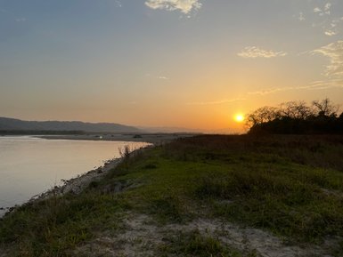 Ein malerischer Sonnenuntergang über einem ruhigen Fluss, umgeben von sanften Hügeln und üppigem Grün am Ufer.