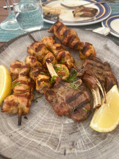 Gegrillte Fleischspieße und Lammkoteletts auf einem rustikalen Teller, garniert mit frischer Petersilie und Zitronenscheiben.