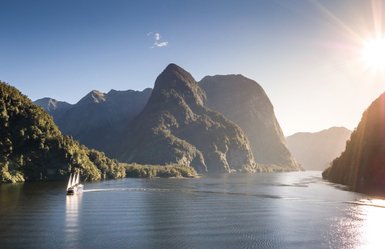 Ein Segelboot gleitet sanft durch das ruhige Wasser des Doubtful Sound, umgeben von majestätischen Bergen und üppigem Grün.