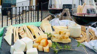 Ein rustikales Käsebrett mit verschiedenen Käsesorten, Brotsticks und Rotwein, umgeben von einer malerischen Kulisse.