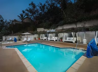 Ein einladender Poolbereich mit bequemen Liegen und Sonnenschirmen, umgeben von üppigem Grün und einem klaren Himmel.