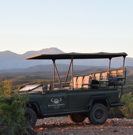 Ein Jeep mit offenen Sitzen steht in der Wildnis, umgeben von sanften Hügeln und Bergen im Hintergrund.