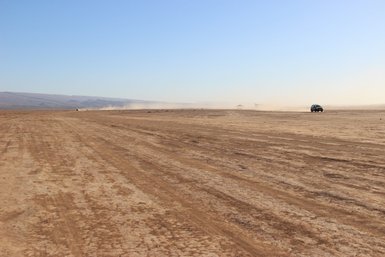 Ein Jeep fährt über eine staubige, weite Landschaft, umgeben von sanften Hügeln und klarem Himmel.