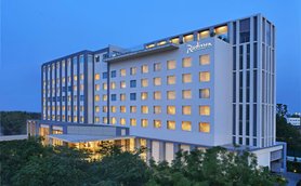 Das Radisson Hotel in Agra strahlt in der Dämmerung mit beleuchteten Fenstern und modernem Design, umgeben von Bäumen.