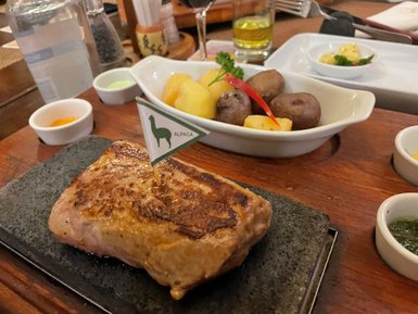 Ein saftiges Stück Alpaka-Fleisch auf einem heißen Stein, garniert mit einer kleinen Fahne und verschiedenen Saucen.