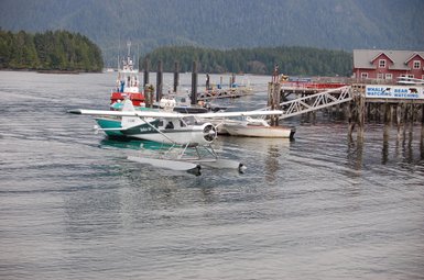 Ein Wasserflugzeug gleitet sanft über die ruhige Wasseroberfläche in einem malerischen Hafen mit Booten und einem Steg.