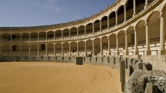 Die Arena zeigt eine leere Stierkampfarena mit sandigem Boden und eleganten Bögen, die die Zuschauerplätze umgeben.
