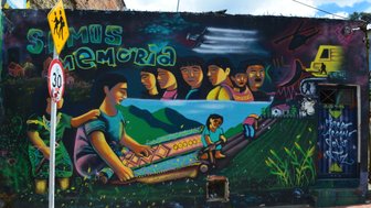 Ein lebendiges Wandgemälde zeigt Menschen, die Erinnerungen und Traditionen in einer farbenfrohen Landschaft darstellen.