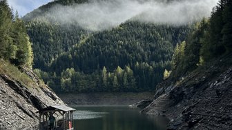 Ein kleines Boot liegt ruhig am Ufer eines klaren Sees, umgeben von majestätischen Bergen und dichten Wäldern.