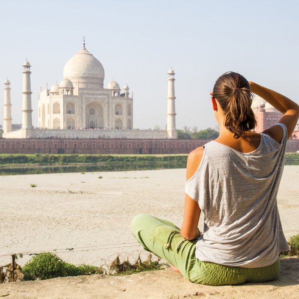 Eine Frau sitzt am Ufer und betrachtet das majestätische Taj Mahal, umgeben von einer ruhigen Landschaft.
