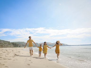 Eine fröhliche Familie in gelben Outfits läuft am Strand entlang, während die Wellen sanft ans Ufer schlagen.