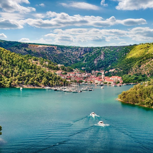Eine malerische Küstenstadt in Kroatien, umgeben von grünen Hügeln und klarem Wasser, mit Segelbooten im Hafen.