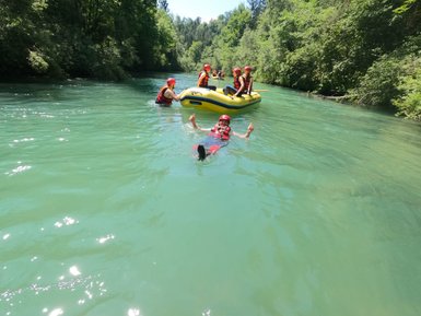 Eine Gruppe von Menschen in roten Helmen paddelt in einem gelben Schlauchboot auf einem klaren, grünen Fluss.