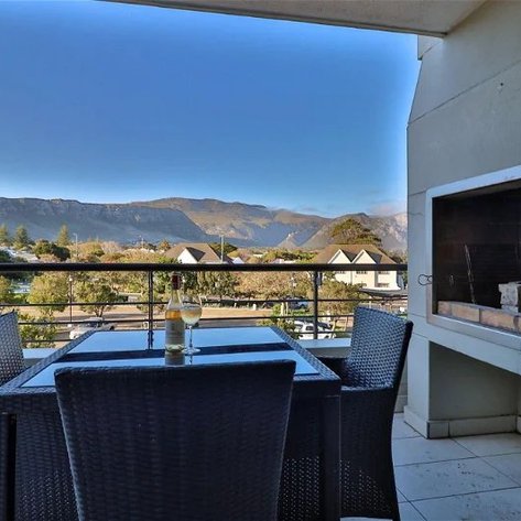 Ein eleganter Balkon mit einem Tisch und Stühlen, Blick auf die Berge und eine Feuerstelle im Hintergrund.