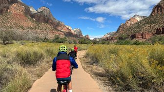 Drei Radfahrer in bunten Helmen fahren auf einem Weg durch die beeindruckende Landschaft des Zion Nationalparks.