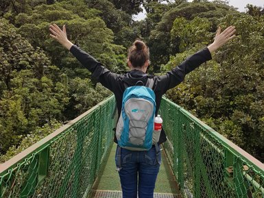 Eine Frau überquert eine Hängebrücke hoch über dem Boden im tropischen Regenwald – Costa Rica Reise mit Kindern
